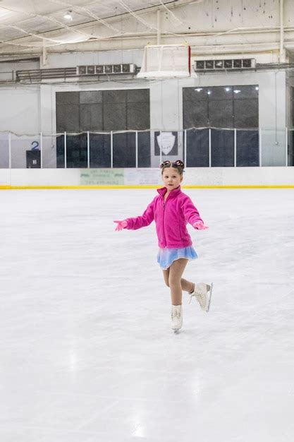 Menina praticando patinação artística em uma pista de gelo coberta