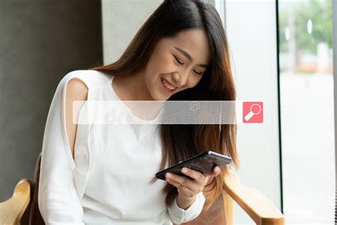 Asian Woman Sitting In Coffee Shop And Using A Smartphone For Searching