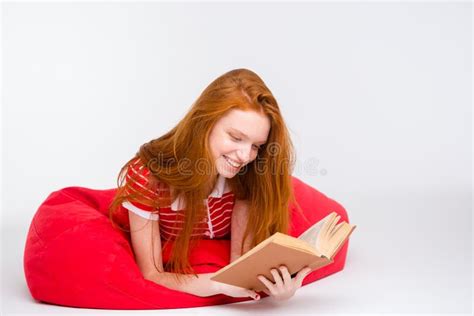 Beautiful Smiling Woman Lying On Bean Bag And Reading Book Stock Photo