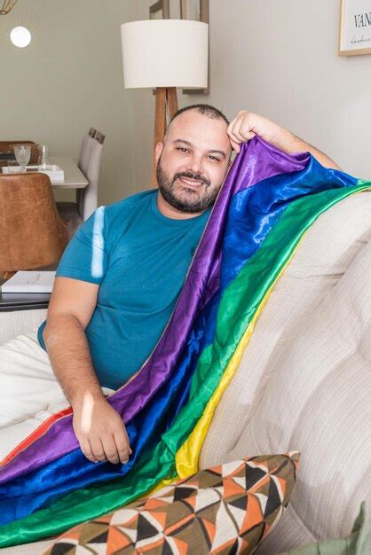 Hombre gay sentado en un sofá en casa con bandera lgbt Foto Premium