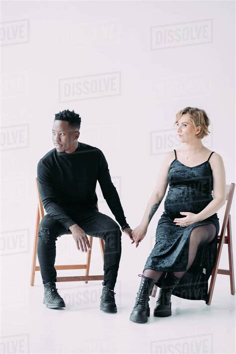 Young African Man And His Caucasian Pregnant Woman Sit On Chairs And