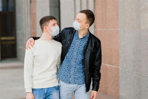 Pareja gay joven con máscara médica abrazándose en la ciudad Foto Premium