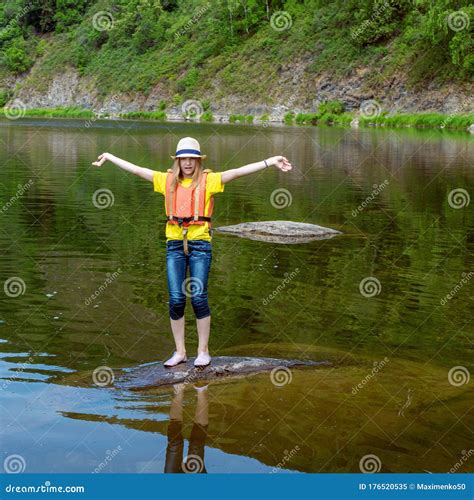 Young Girl In Life Jacket Standing On Stone In Water Waving Hands