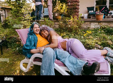 Happy Gay Man With Transwoman Lying Down On Chair During Party In Back Yard Stock Photo Alamy