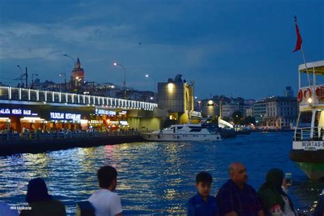 People Are Sitting On The Edge Of A River Watching Boats Pass Under A