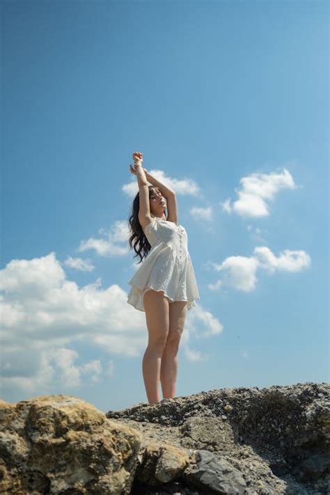 Young Woman In A White Dress Standing On A Rock Under Blue Sky · Free