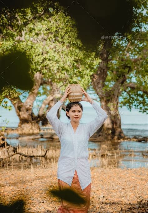 country girl in traditional clothes at beach in summer season with mangrove trees in background ...