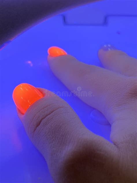 Female Hand With Neon Orange Manicure Inside A Blue Uv Lamp Drying Gel