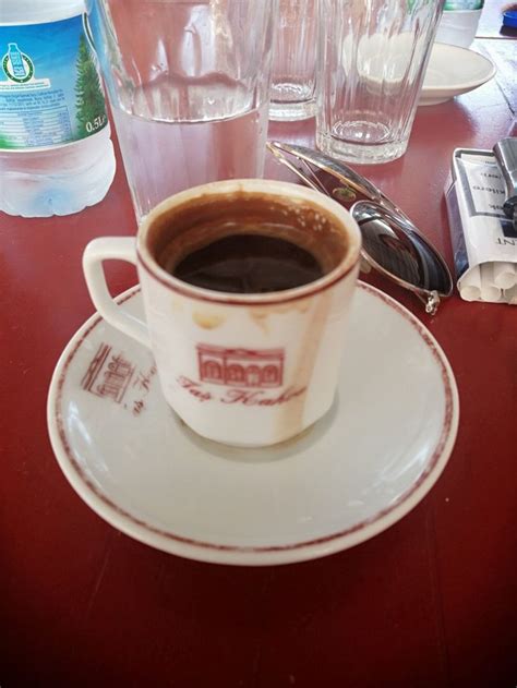 A Cup Of Coffee Sitting On Top Of A Saucer Next To Glasses And Spoons