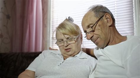 An Adult Couple Looks At Their Photos Sitting At Home On The Couch