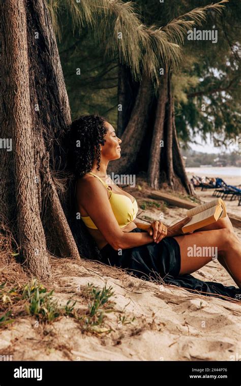 Side View Of Mature Woman Reclining On Tree Trunk With Book At Beach Stock Photo Alamy