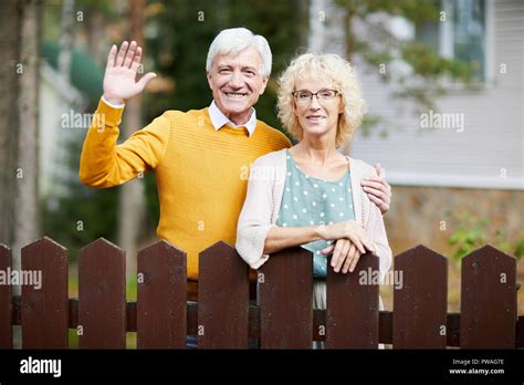 Hospitable Mature Couple Standing By Fence While Friendly Man Waving