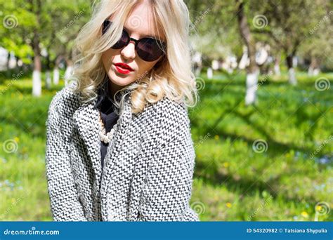Belle Jeune Fille Blonde Heureuse Dans Le Manteau Les Jeans Et Des Lunettes De Soleil Photo