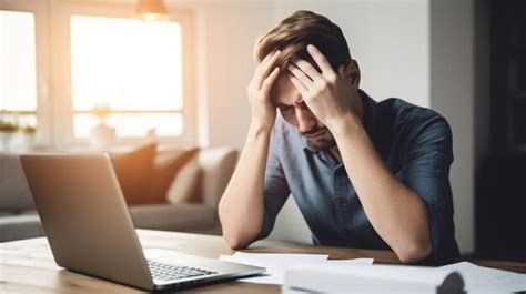 Um homem está sentado em uma mesa um laptop e a cabeça entre as