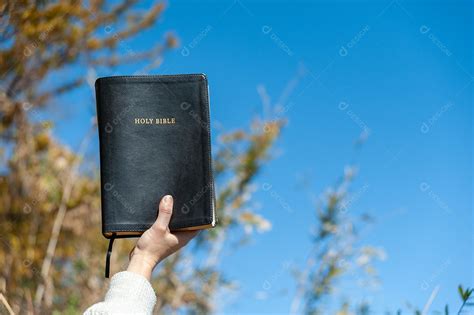 Mão levantada segurando a Bíblia Sagrada Fundo árvores e céu azul