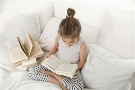 Cute little girl reading a book on the bed in the bedroom. | Free Photo