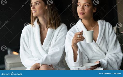 Lesbian Couple Relaxing And Drinking Tea In Robes During Wellness