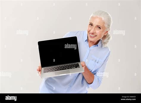 Beautiful Mature Grey Haired Woman Smiling And Showing Blank Screen Of Laptop Computer Isolated