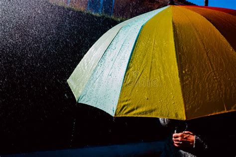 Rain Falls On An Umbrella Among Sun Rays Dark Background In Black