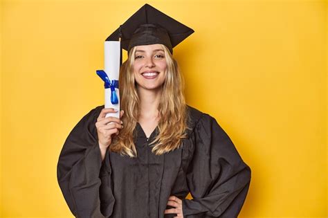 Jovem graduada de boné e vestido segurando um diploma em um estúdio