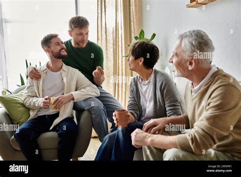 A Gay Couple Sits With Parents In Their Living Room Enjoying A Conversation And Drinks Stock