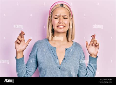 Beautiful Blonde Woman Standing Over Pink Background Gesturing Finger Crossed Smiling With Hope