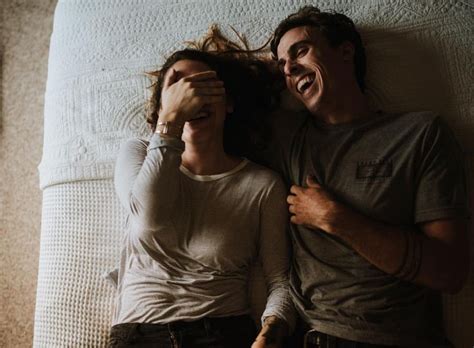 Two People Laying On Top Of A Bed With Their Arms Around Each Other And Smiling