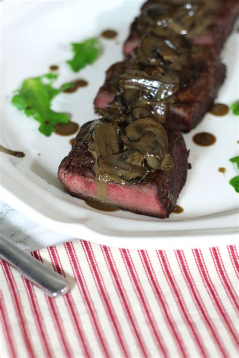 A Piece Of Steak Covered In Mushrooms On A White Plate With A Red And White Striped Napkin