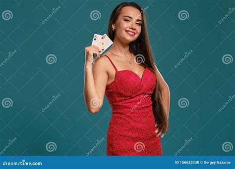 Brunette Girl With A Long Hair Wearing A Red Dress Is Posing Holding Two Playing Cards In Her