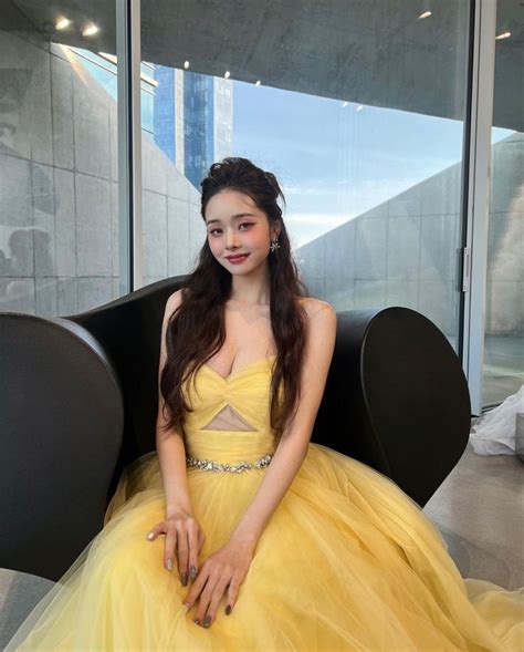 A Woman In A Yellow Dress Is Sitting On A Black Chair And Posing For