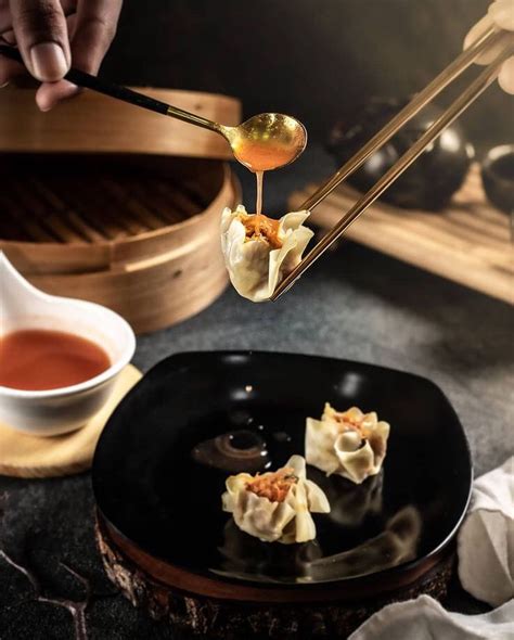 Someone Is Dipping Sauce On Some Dumplings In A Black Plate With Chopsticks