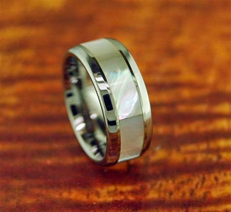 A Wedding Band With A White Mother S Day Pearl In It On A Wooden Surface