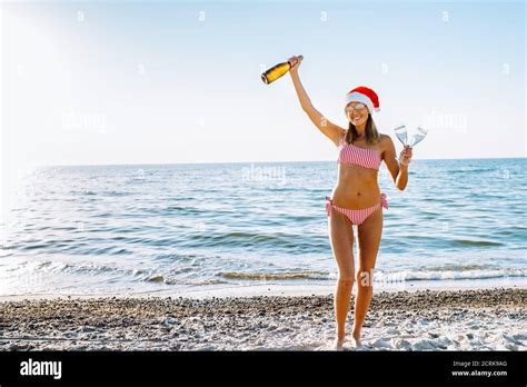 Belle femme blonde en bikini rouge et blanc et chapeau de père Noël avec champagne sur une plage
