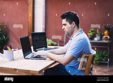 Man Sitting On A Garden Terrace Using Two Laptops To Trade In