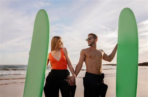 Couple De Jeunes Surfeurs Se Tenant La Main Et Posant Avec Des Planches