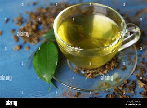 Glass Cup Of Tea With Green Leaves And Scattered Tea Around On Blue