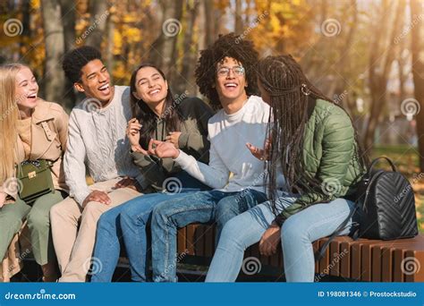 Teenagers Having Fun At Public Park Sitting On Bench Talking Stock