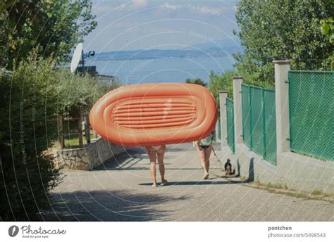 Two Women In Bikini Carry Orange Inflatable Boat In A Royalty Free