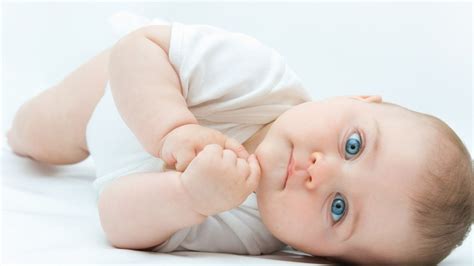 Cute Blue Eyes Baby Is Lying Down On Floor Wearing White Dress In White