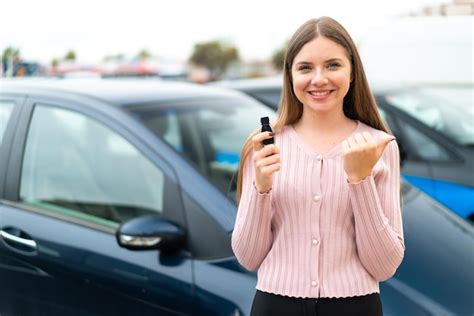 Jeune Jolie Femme Blonde Tenant Des Clés De Voiture à L extérieur Pointant Vers Le Côté Pour