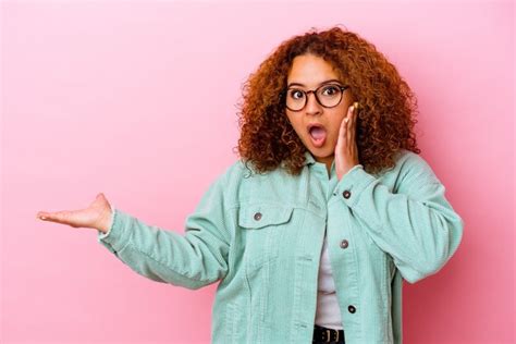 Jovem latina curvilínea isolada na parede rosa impressionada segurando o espaço da cópia na