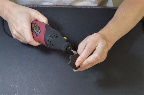 A Person Using A Power Drill On A Black Table With A White Shirt Behind It