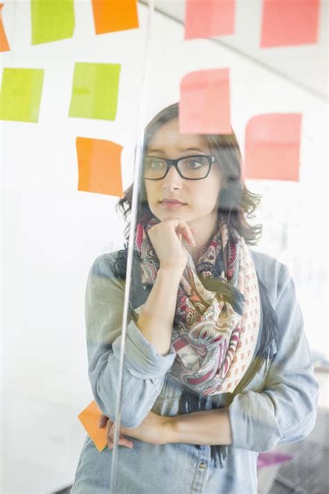 Creative Businesswoman Reading Sticky Notes On Glass Wall In Office