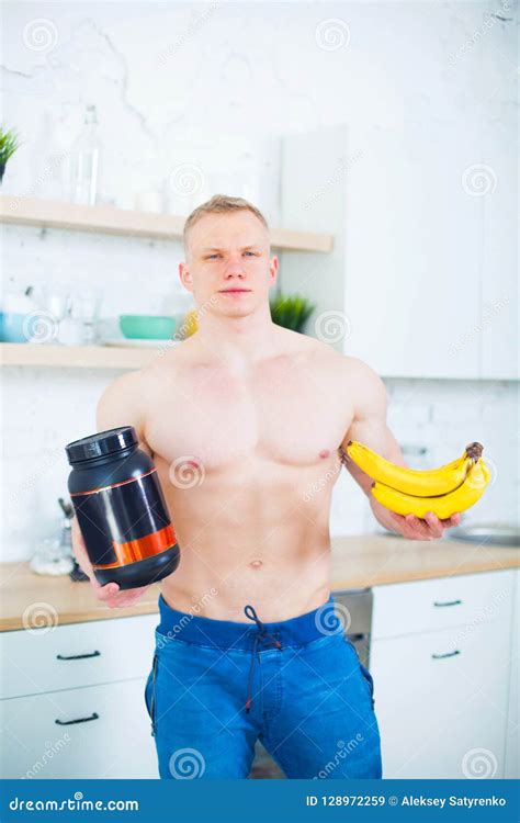 Muscular Man With A Naked Torso In The Kitchen With A Sports Nutrition Protein And Bananas The