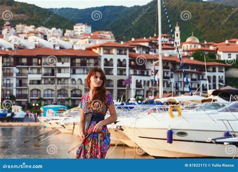 Attractive Brunette In Long Colorful Dress Standing Alone On The Beach Against The Backdrop Of