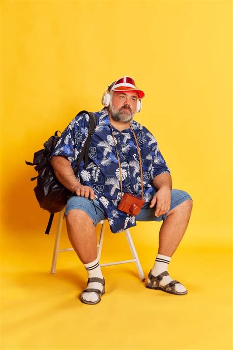 Portrait Of Fat Mature Man In Stylish Shirt Cap With Backpack Sitting With Bored Face Posing
