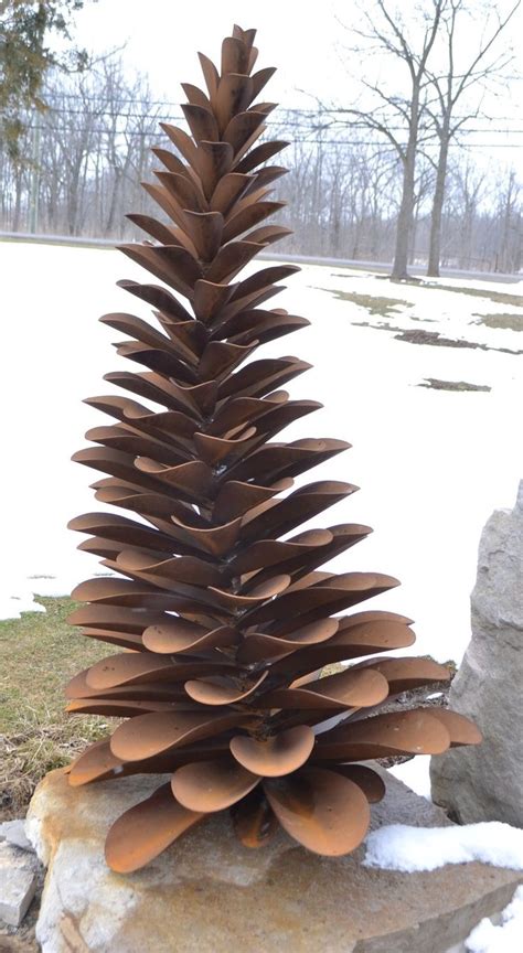 A Large Metal Pine Cone Sitting On Top Of A Pile Of Rocks In The Snow