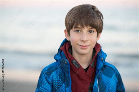 Young boy posing at the winter beach. Cute smiling happy 11 years old boy at seaside, looking at ...