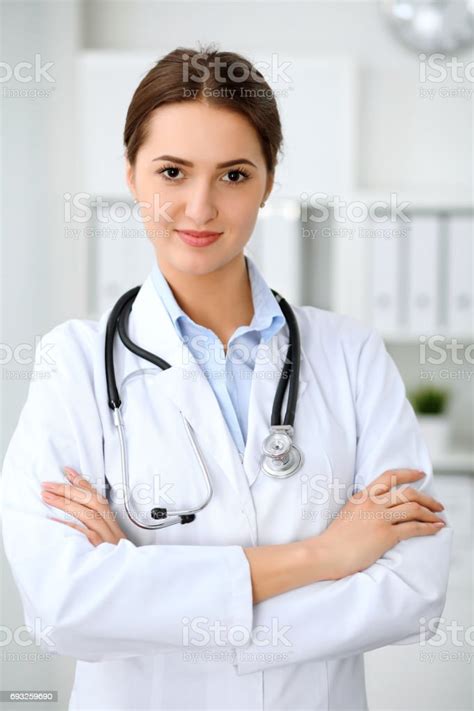 Young Brunette Female Doctor Standing With Arms Crossed And Smiling At