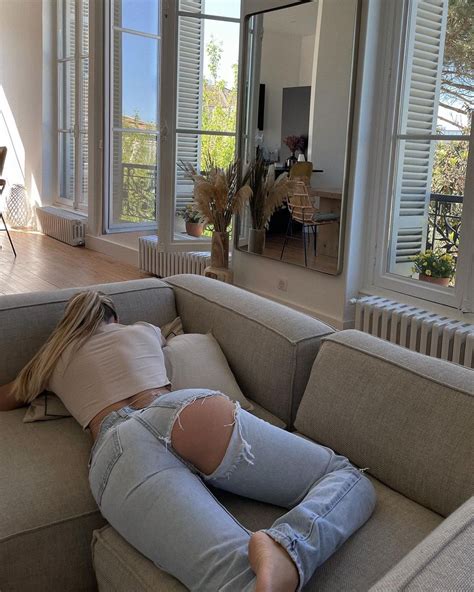 A Woman Laying On Top Of A Couch In A Living Room Next To A Window